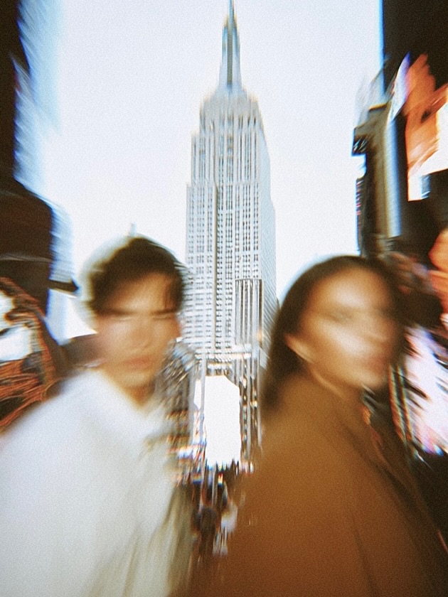 Two figures walking past camera, the Empire State Building lit behind them